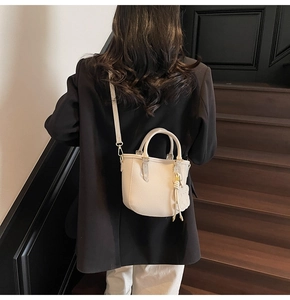 Rear view of model with white mini leather bucket bag and a bear charm on wooden stairs