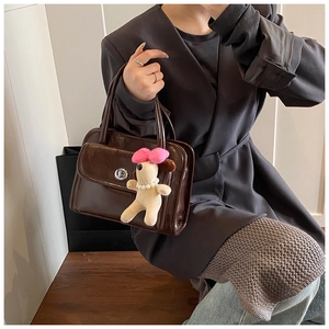 Close-up of a glossy dark brown handbag featuring a silver clasp and a cute plush dog charm