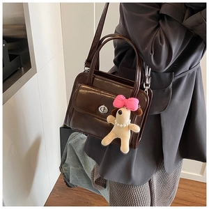 Detailed view of brown leather handbag with silver twist lock and plush puppy charm