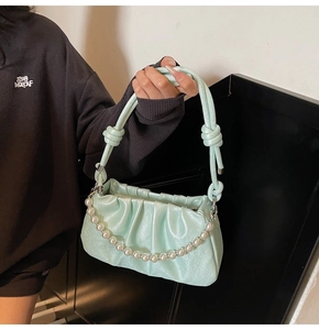 Close-up of light green pleated cloud bag with elegant pearl chain and knotted strap