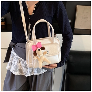Detail of cream pleated leather handbag featuring a cute plush puppy charm and metal twist lock