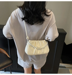 Detail of cream white pleated crossbody bag with decorative pearl chain and knotted strap