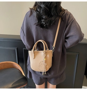 Detail of khaki leather bucket bag with dog embossed design and metal tassel charm