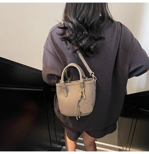 Detail of khaki leather bucket bag with cute dog charm shown on a female model