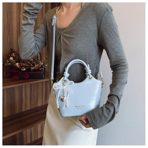 Detail der hellblauen Beuteltasche mit Spitzenschleife und Perlenanhänger am Model
