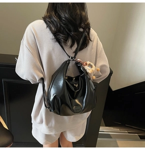 Zaino hobo nero lucido con ciondolo in peluche mostrato a spalla per donna elegante