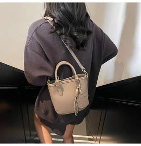 Detail of taupe pebbled leather bucket bag with dog charm on a female model
