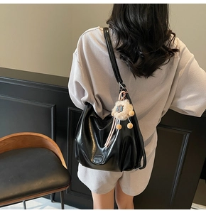 Dettaglio borsa hobo nera lucida con tracolla e ciondolo a forma di leone in peluche