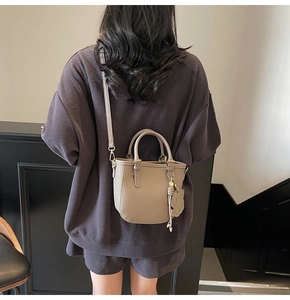Detail of khaki lychee grain leather bucket bag with a cute bear charm on a model