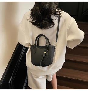 Detail of black lychee grain leather bucket bag with dog pendant on wooden stairs