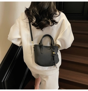 Close-up of black pebble leather bucket bag with dual handles and bear charm detail