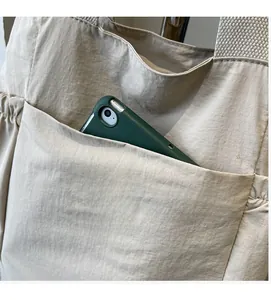 Detail of spacious front pocket on beige nylon tote bag with fashion logo patch