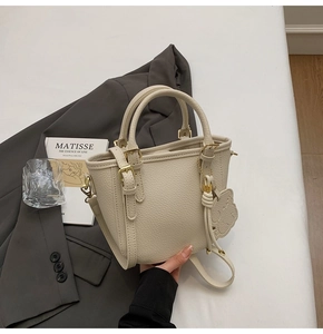 Detail of beige lychee pattern leather bucket bag with gold hardware and kitty charm