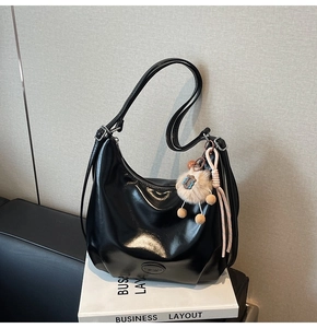 Dettaglio borsa a spalla nera lucida con ciondolo a forma di agnello e logo del marchio