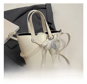 Détail du sac seau blanc en cuir ciré avec nœud en dentelle et breloques en perles sur veste