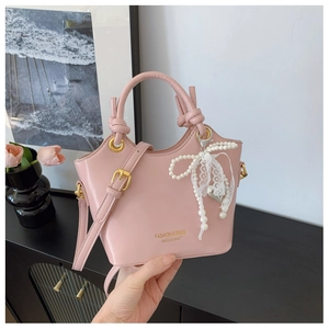 Detail einer hellrosa Handtasche mit Perlen-Schmetterlingsanhänger und goldenem Schriftzug