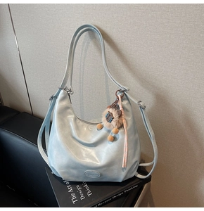 Dettaglio borsa hobo celeste con ciondolo a orsetto sopra un libro di design