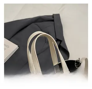 Détail du sac seau blanc cassé avec doubles poignées, coutures fines et breloque dentelle