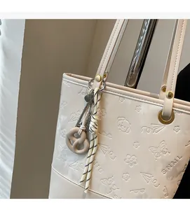 Dettaglio della borsa tote beige con motivi a farfalla in rilievo e ciondolo alla moda