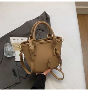 Detailed macro view of khaki lychee grain leather handbag with dog-shaped charm