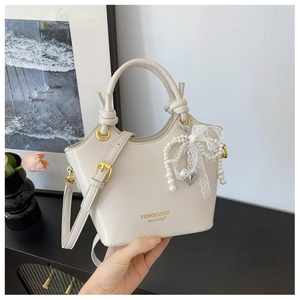 Detail der cremeweißen Eimertasche mit Perlen-Spitzenschleife und Herz-Anhänger