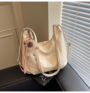 Dettaglio di una borsa hobo in pelle lucida bianco crema con un simpatico ciondolo peluche