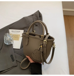 Close-up of tan lychee textured handbag with golden hardware and cute dog embossed detail