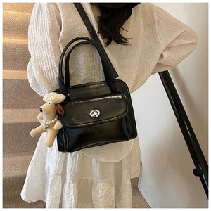 Detail of black glossy handbag with silver twist lock and cute white plush dog charm