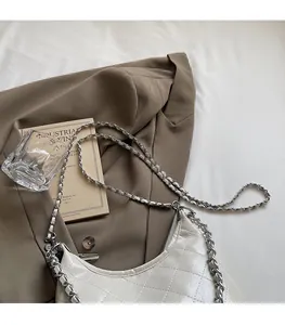 Detail der gesteppten cremeweißen Kunstledertasche mit silberner Kette auf dem Blazer