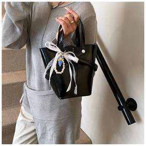 Détail d'un sac seau noir en cuir avec nœud en dentelle blanche et breloque en perles