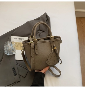 Detail of taupe lychee texture leather bucket bag with gold hardware and dog charm