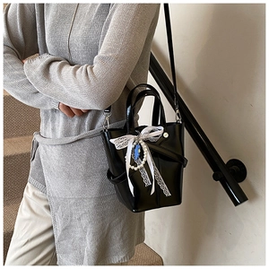 Détail du sac seau en cuir verni noir avec nœud en dentelle et chaîne de perles