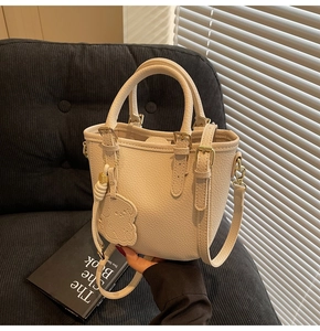 Detail of cream white pebbled leather bucket bag with gold hardware and bear charm