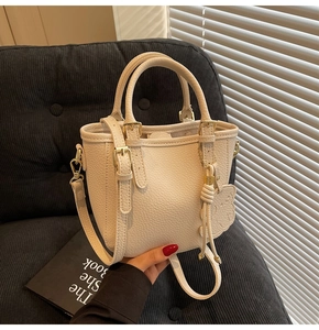 Detail of cream white lychee leather bucket bag with gold hardware and bear charm