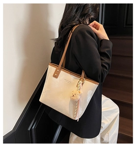 Detail of a minimalist two-tone bucket bag with plush bear charm on office steps