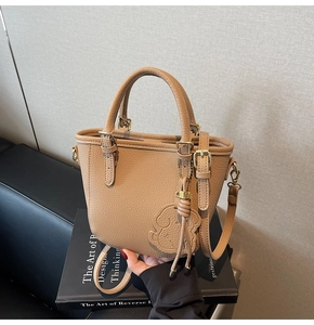 Detail of khaki leather bucket bag with dog charm and gold hardware on book