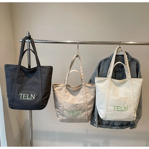 Detail of canvas tote bags with front pockets and TELN embroidery in various colors
