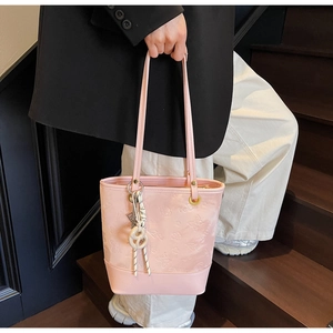 Dettaglio della borsa rosa con goffratura floreale e ciondoli su una scala in legno