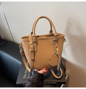 Detail of brown leather bucket bag featuring a cute dog charm and polished gold hardware