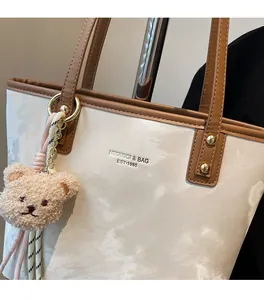 Detail of a large cream tote bag with brown handles and a cute plush bear pendant accessory