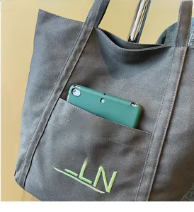 Close-up of deep gray canvas tote bag featuring an outer pocket and green TELN embroidery