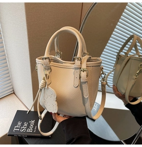 Detailed macro view of cream-colored lychee leather bucket bag with cute bear charm detail