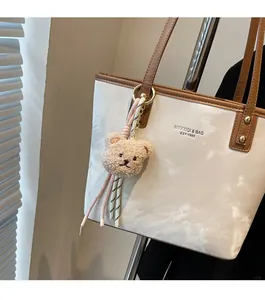 Detail of white marble tote bag with brown straps and a cute plush bear charm accessory