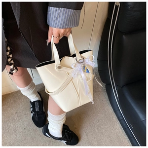 Détail du sac seau en cuir ciré crème avec nœud en dentelle et pendentif perle