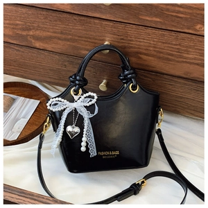 Detail einer schwarzen Lackhandtasche mit Perlenbogen und goldenem Herzanhänger