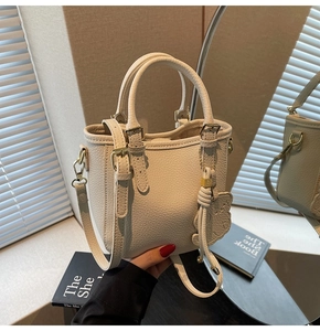 Close-up of cream mini bucket bag with pebbled texture and cute cat charm in mirror reflection