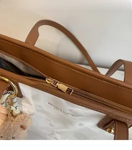 Detail of golden zipper and brown leather trim on the white textured tote bag