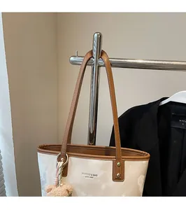 Detail of cream bucket bag showing leather straps, metal buckles and plush bear charm