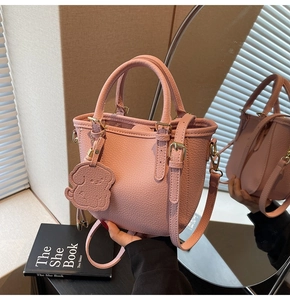 Detail of pink lychee leather bucket bag with cute dog charm and golden hardware