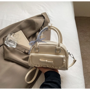 Detail van een beige handtas met strik, kant en blauw-wit geblokt lint om het handvat